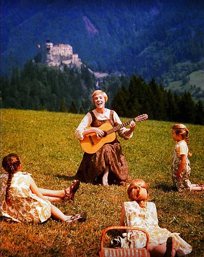 woman playing guitar with children in Swiss Alps with castle in background 