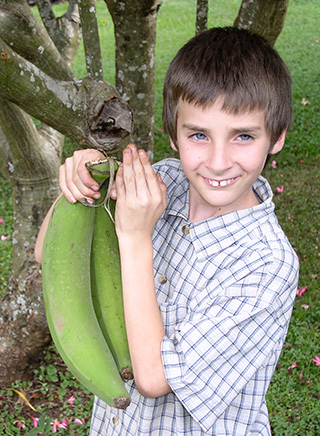photo of boy holding large bananas