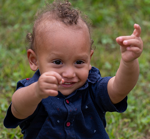 photo of 18 month old boy with curly brown hair with hands reaching out toward photographer