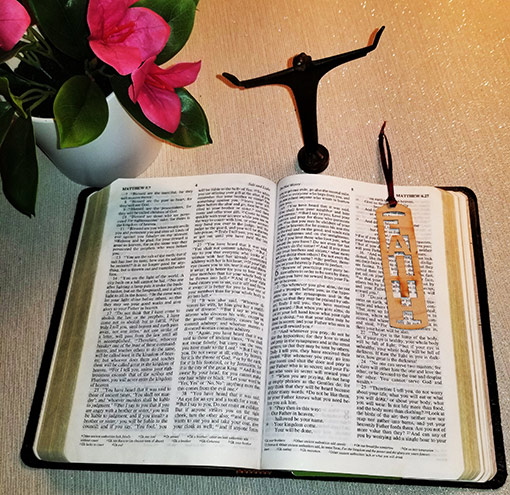 open Bible on table with vase of pink flowers and crucifix