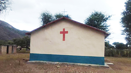 side view of white church in Kenya with blue stripe at bottom and red cross at center top