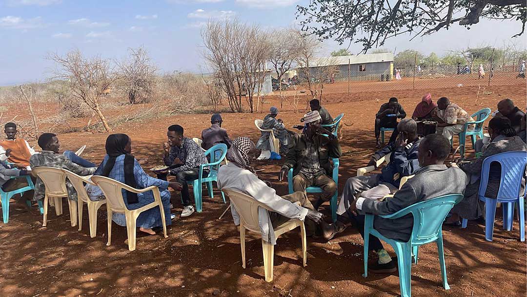 group of men sitting on plastic chairs in shade of tree in Kenya
