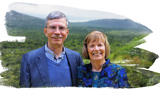 man wearing blue shirt, vest & jacket, woman wearing blue blazer with jungle and mountains in background