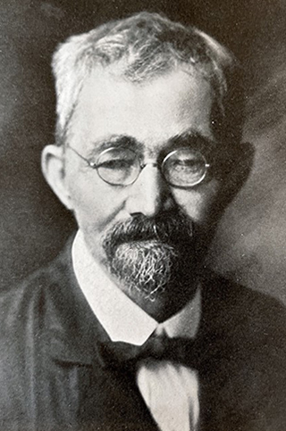 vintage photo of man with Van Dyke beard and mustache, wearing round glasses and old fashioned suit and tie