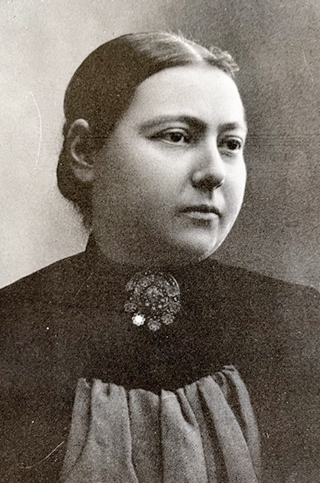 vintage photo of woman with hair pulled back in a bun, wearing black dress and large brooch at neck