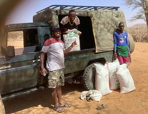 3 Kenyan men by dark gree Land Cruiser unloading food supplies