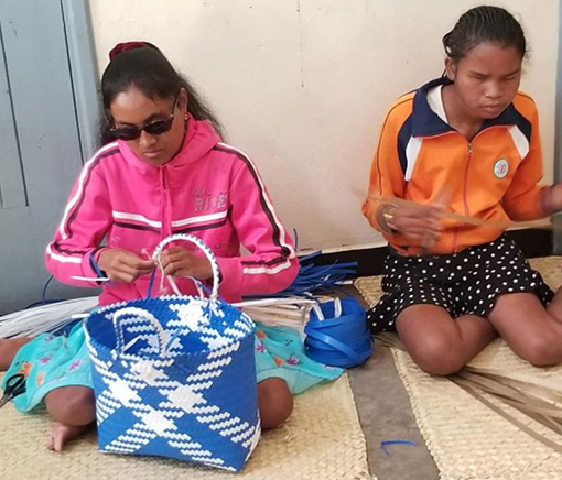 two blind Madagascar girls sitting on woven mat as they weave baskets