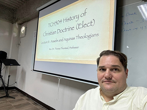 man in white shirt standing by a slide on a projection screen