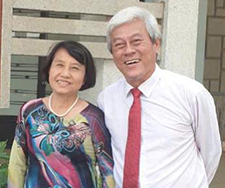 woman with short, dark hair wearing floral dress and man with white hair wearing white shirt and red tie