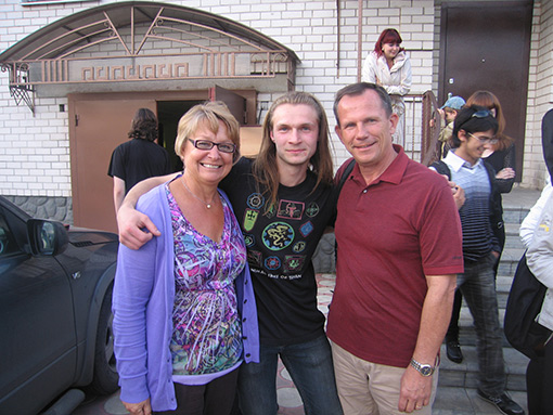 Young man dressed in black standing between woman in purple shirt & sweater and man wearing red shirt