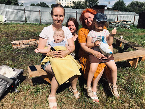 2 women and 3 young children sitting on bench outside