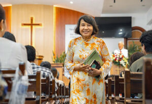 woman in floral dress holding books in aisle of church in Vietnam