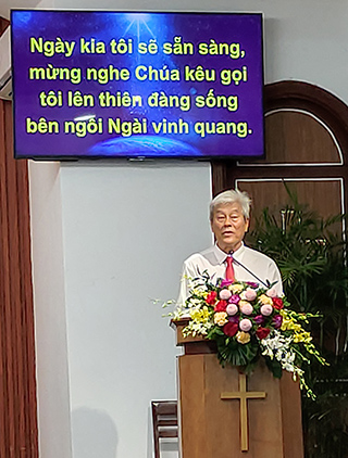 man wearing white shirt and red tie speaking behind pulpit in church in Vietnam