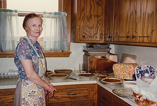 woman wearing blue dress and patterned apron standing in her kitchen
