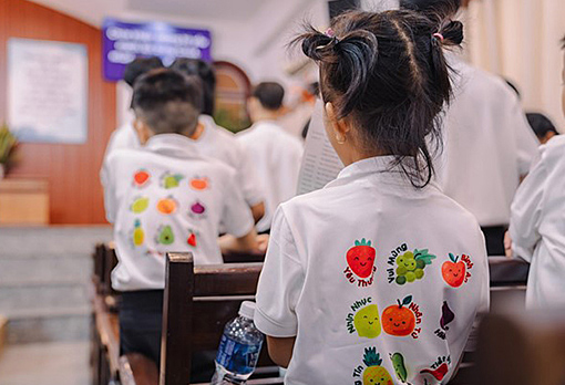 back view of children wearing white shirts with colorful designs in pews of Vietnamese  church