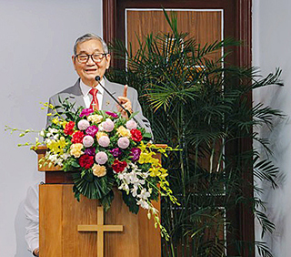 Vietnamese man in suit standing behind flowers on pulpit in church