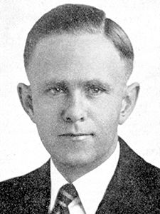 headshot of man wearing black suit and white shirt