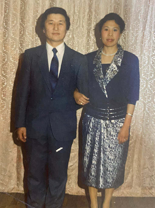 Mongolian husband wearing navy suit and tie with wife wearing stylish print dress with navy jacket