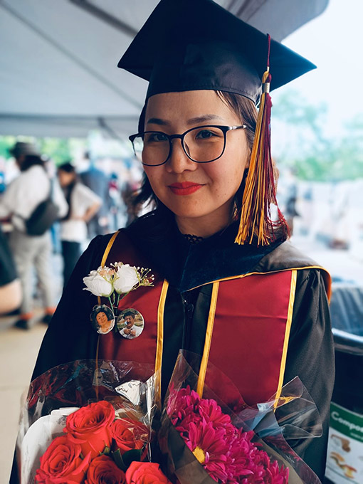 woman graduating from college wearing cap and gown with red honor banner holding bouquet of flowers