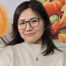 woman with dark hair wearing glasses sitting in front of autumn background