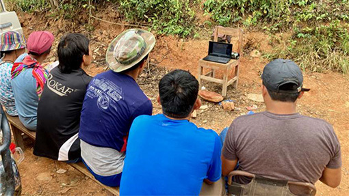 group of people sitting on hillside watching computer screen