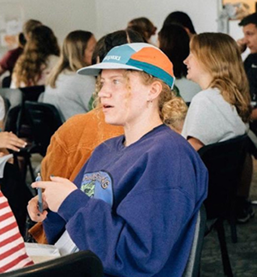girl wearing blue sweatshirt sitting in classroom with other students