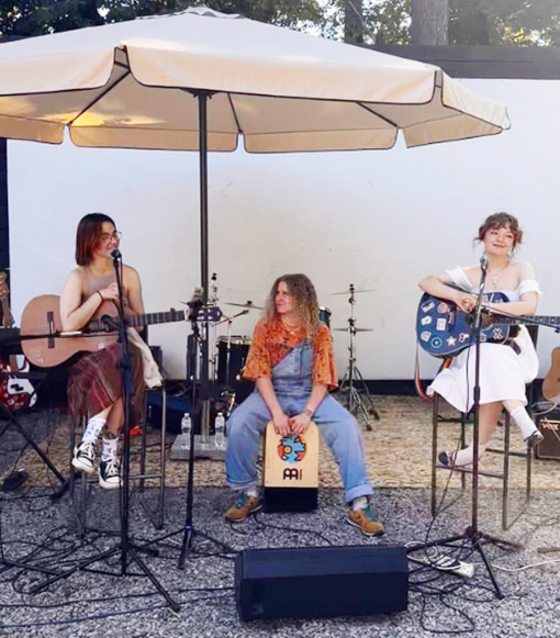 women musicians sitting on stools under umbrella